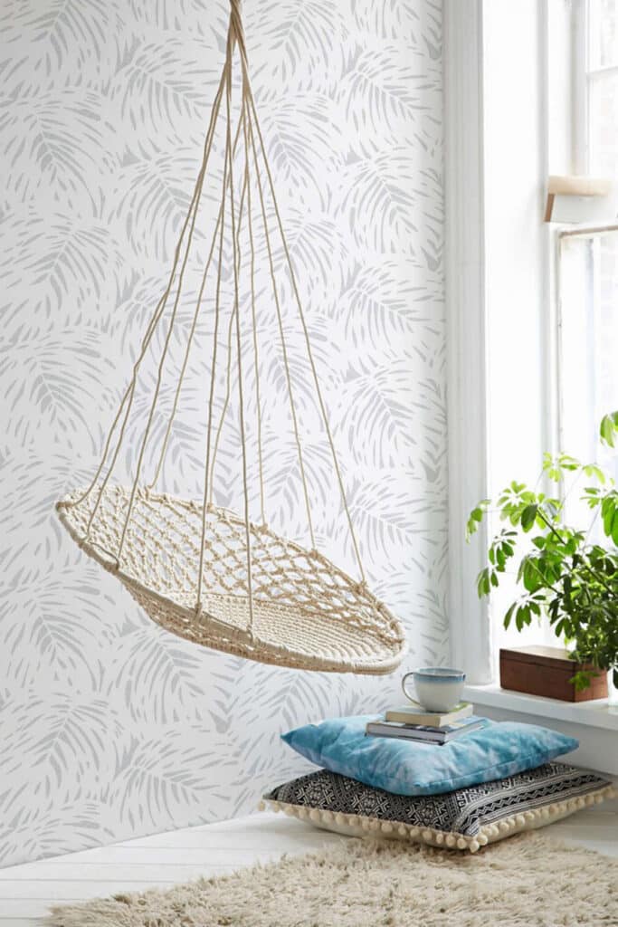 Grey leaf patterned wallpaper with hanging wicker chair in bright room.