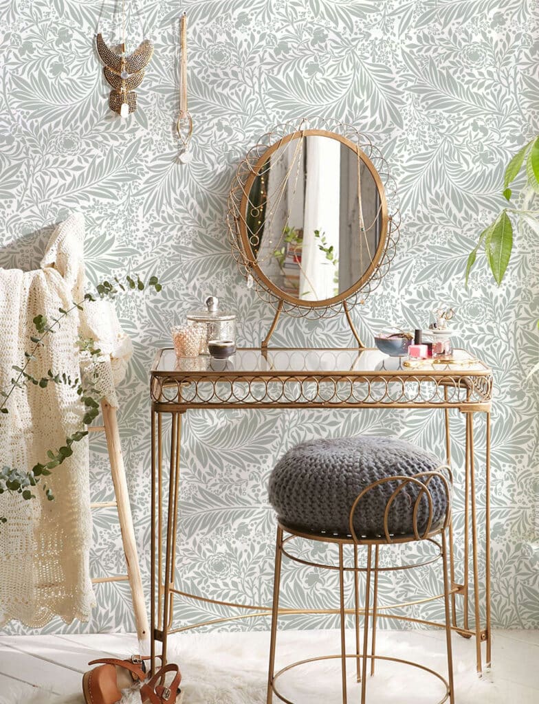 Elegant vanity table with round mirror and cozy stool in a botanical wallpapered room.