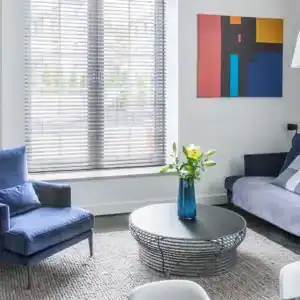 Modern living room with Venetian blinds, abstract art, and stylish furniture.
