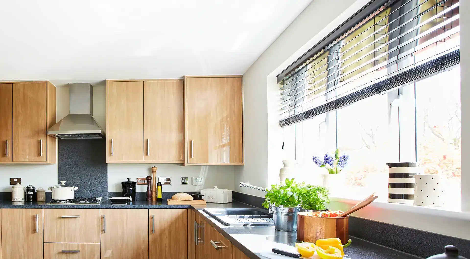 Modern kitchen with wooden cabinets, black countertops, and large window with blinds.